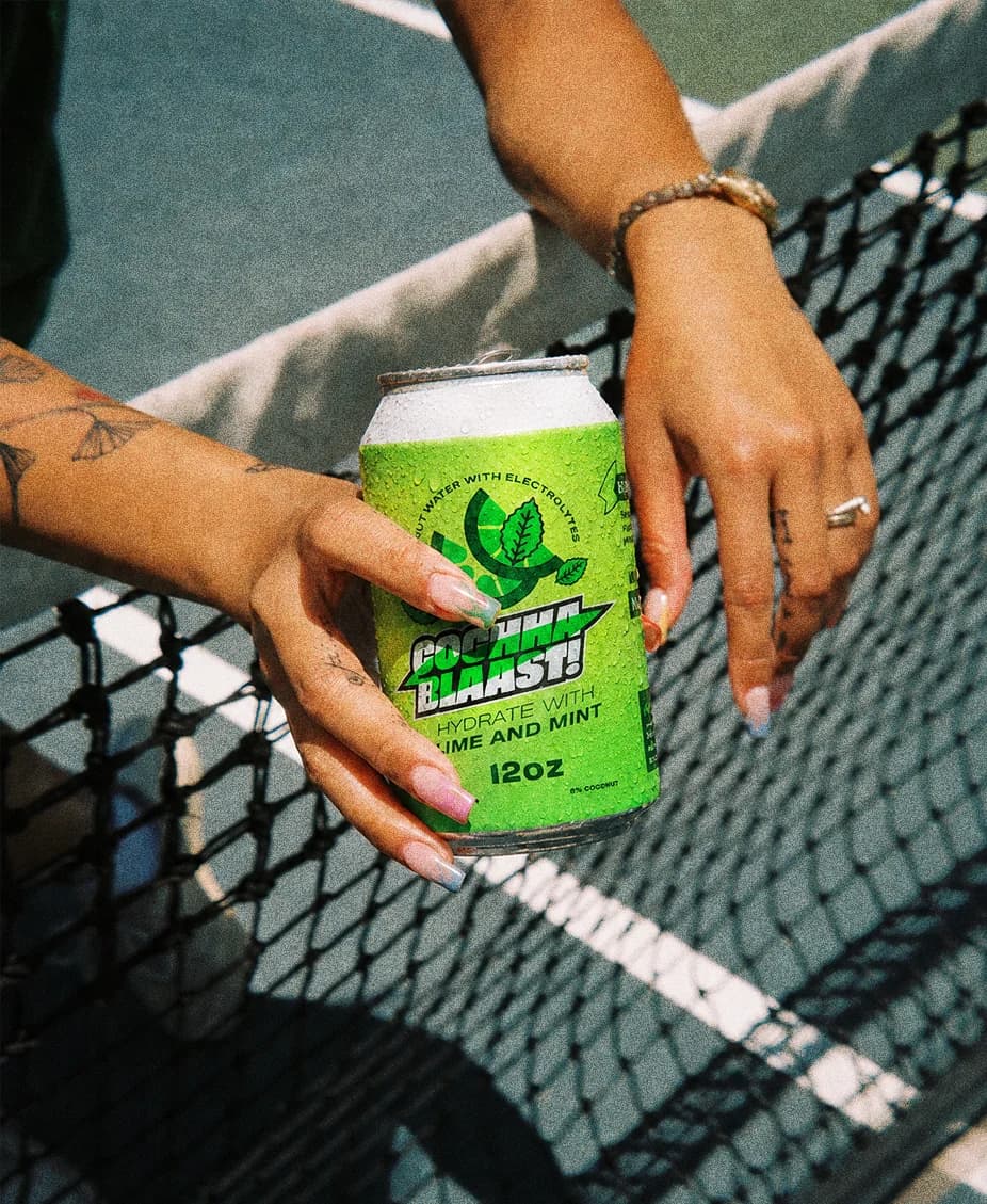 Cochaa Blaast lime and mint can held over a tennis net